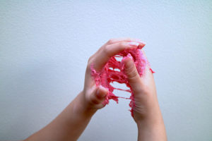 Two hands hold a stretchy, sticky pink substance between them